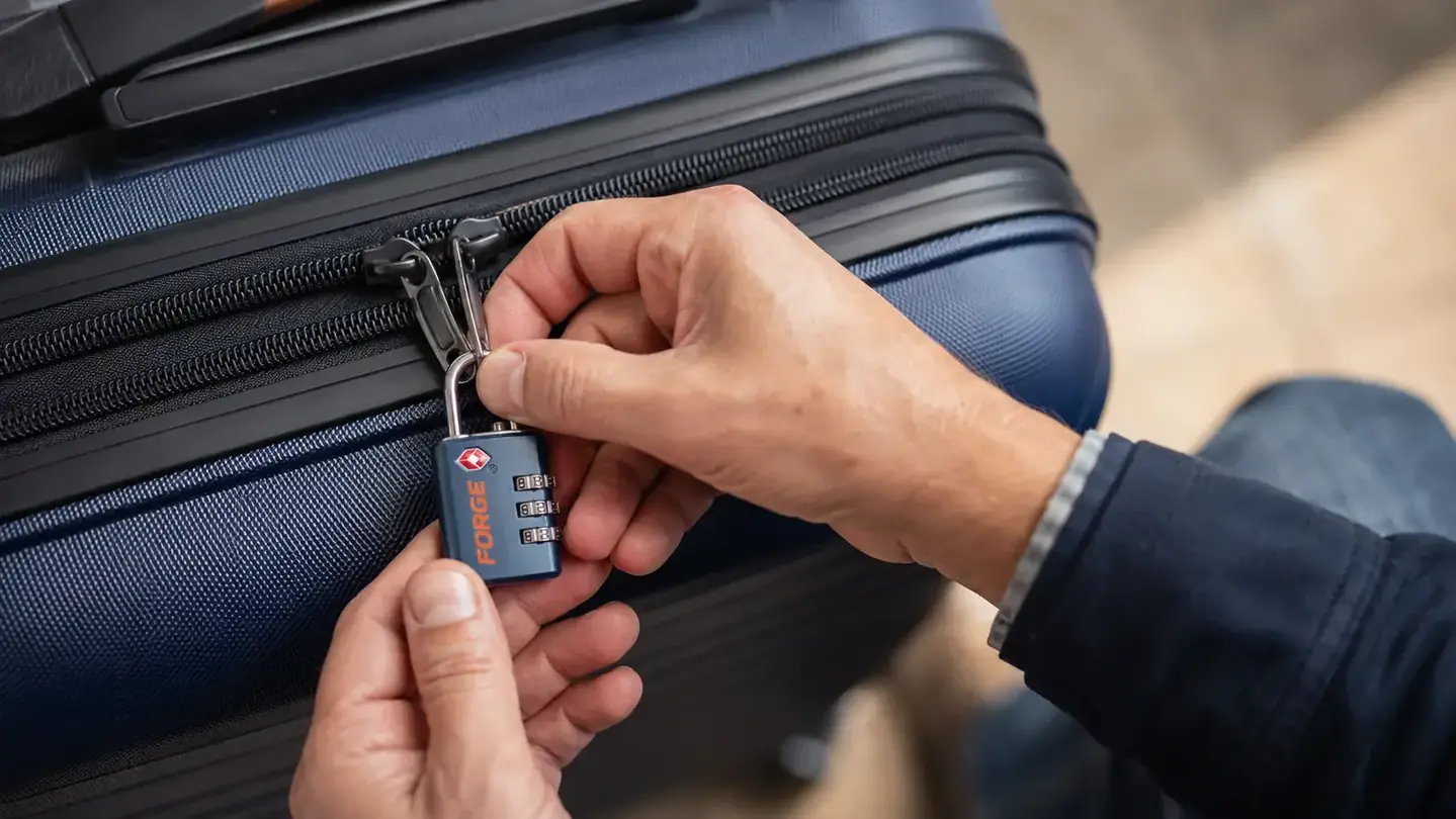 Hand holding a Forge TSA combination lock next to an open suitcase zipper pull