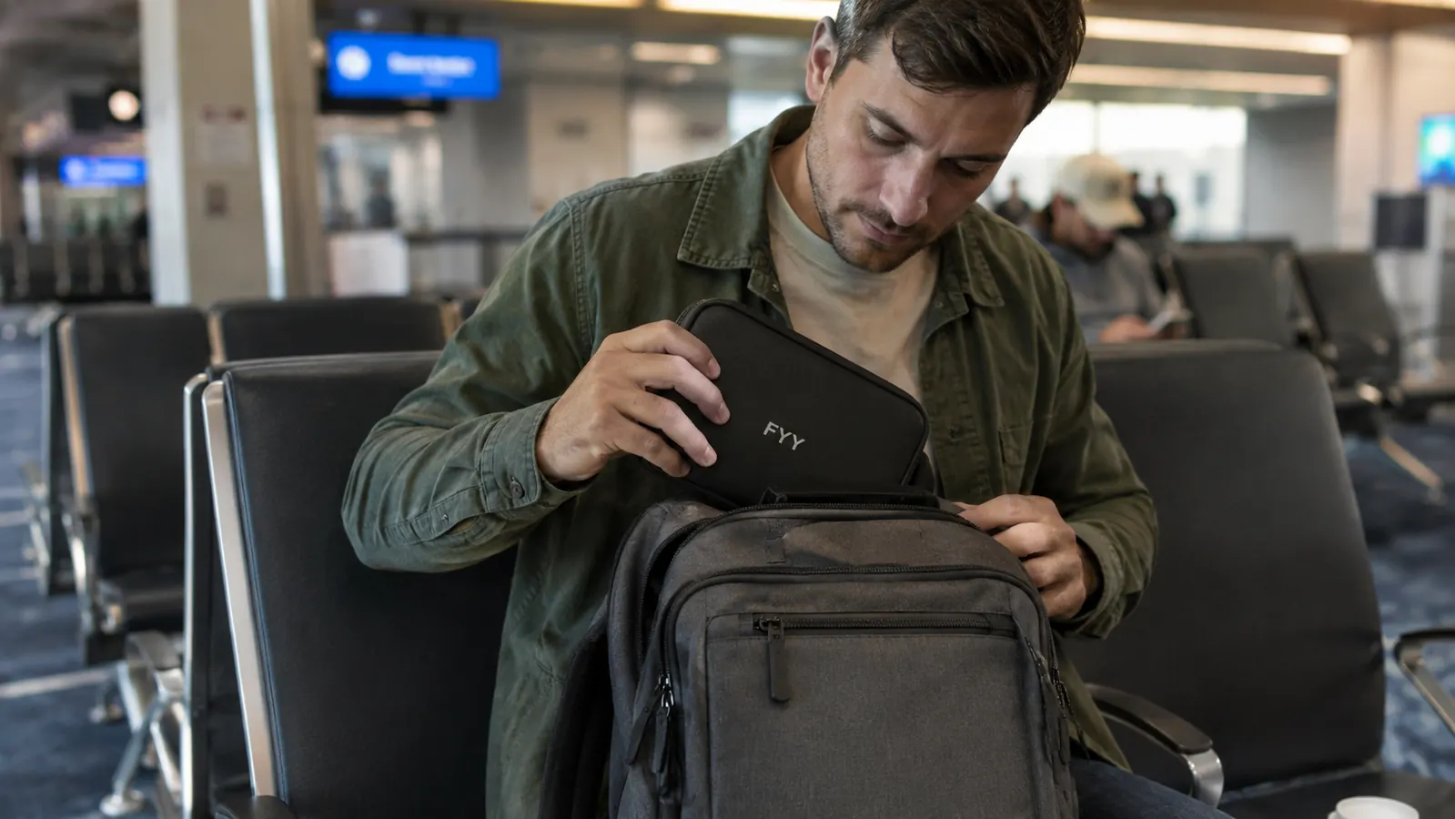 FYY electronics organizer tucked into the front pocket of a gray carry-on backpack at an airport gate