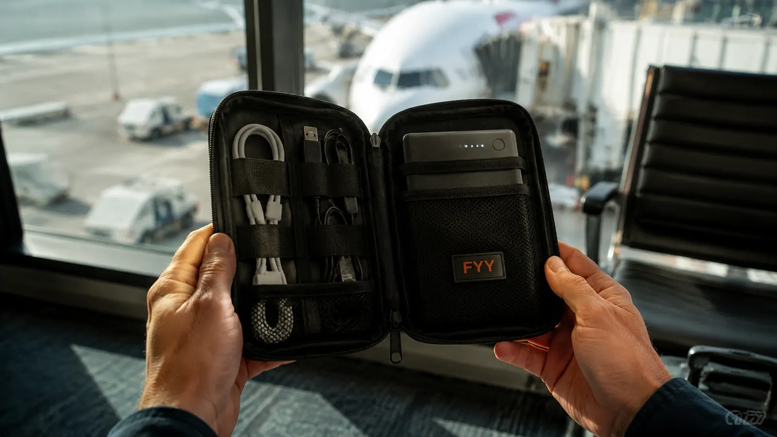 Traveler holding open FYY organizer in one hand at an airport gate, cables and charger visible inside