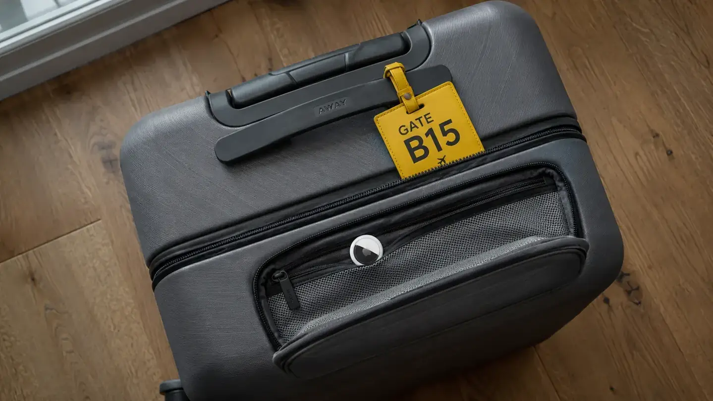 Overhead view of a suitcase packed and closed, with a luggage tag and AirTag tucked in a side pocket